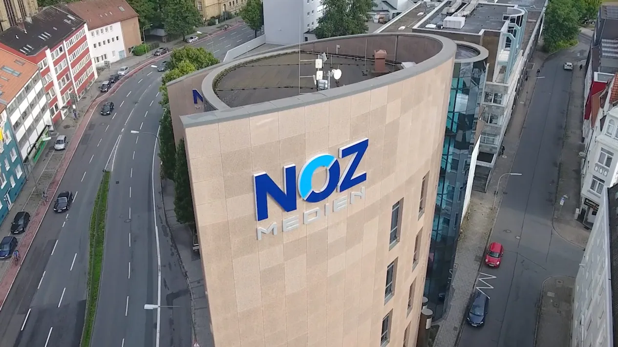 Luftaufnahme des modernen NOZ MEDIEN Gebäudes an einer belebten Straße.