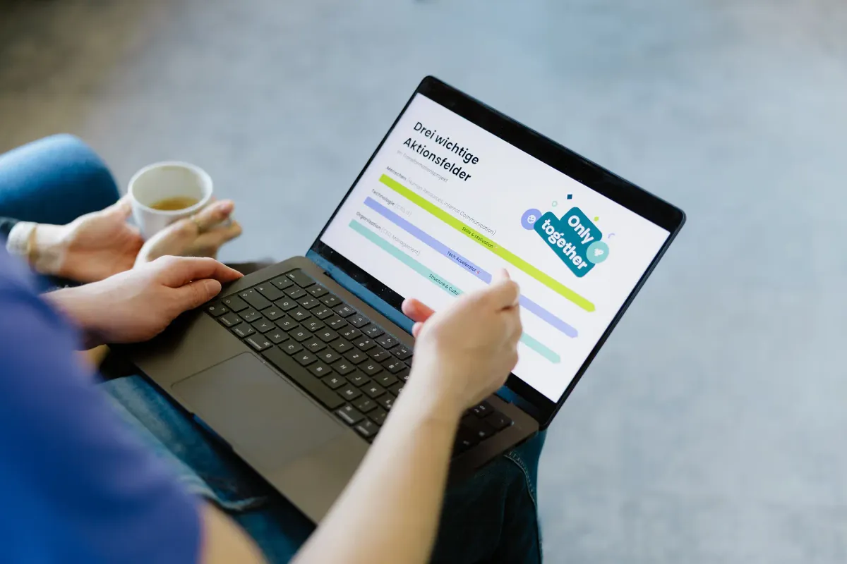 Zwei Personen analysieren in einem Beratungsgespräch eine Präsentation auf dem Laptop, die die drei Aktionsfelder Mensch, Technologie und Organisation zeigt.