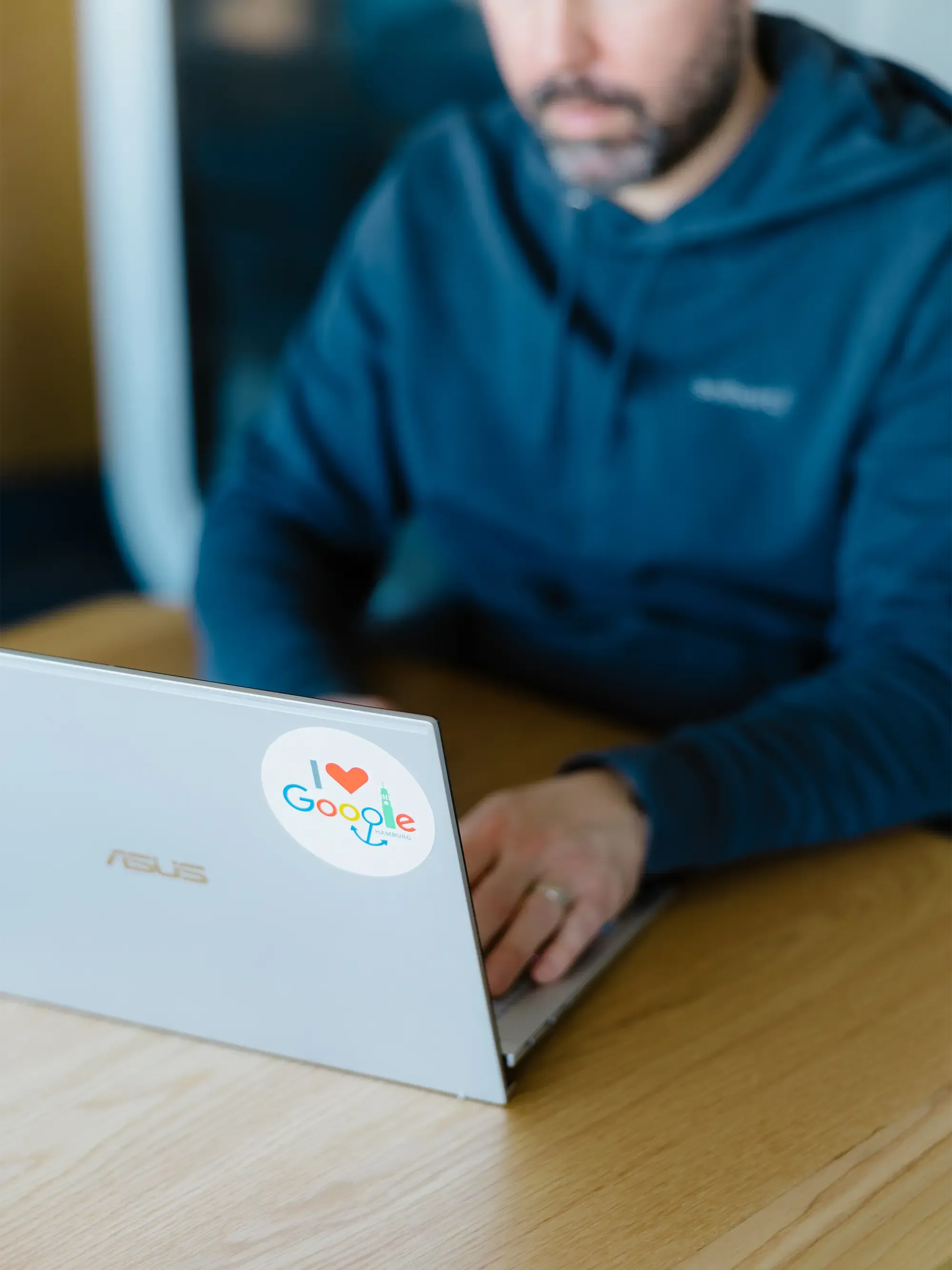 Ein Mann im Hoodie arbeitet an einem Laptop, auf dessen Deckel ein I love Google Aufkleber prangt.