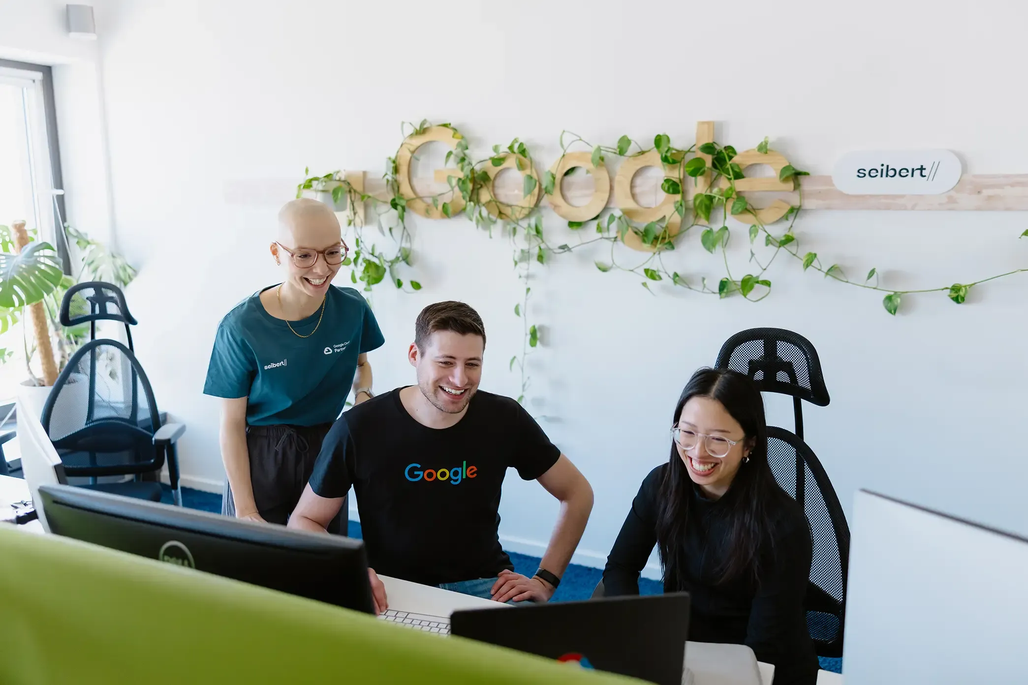 Max, Lisa und Anna arbeiten gut gelaunt gemeinsam an einem Computer im Seibert Büro.