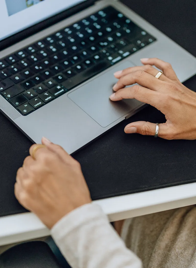Close-up of hands typing on a laptop keyboard, with a focus on the touchpad and screen displaying a document.
