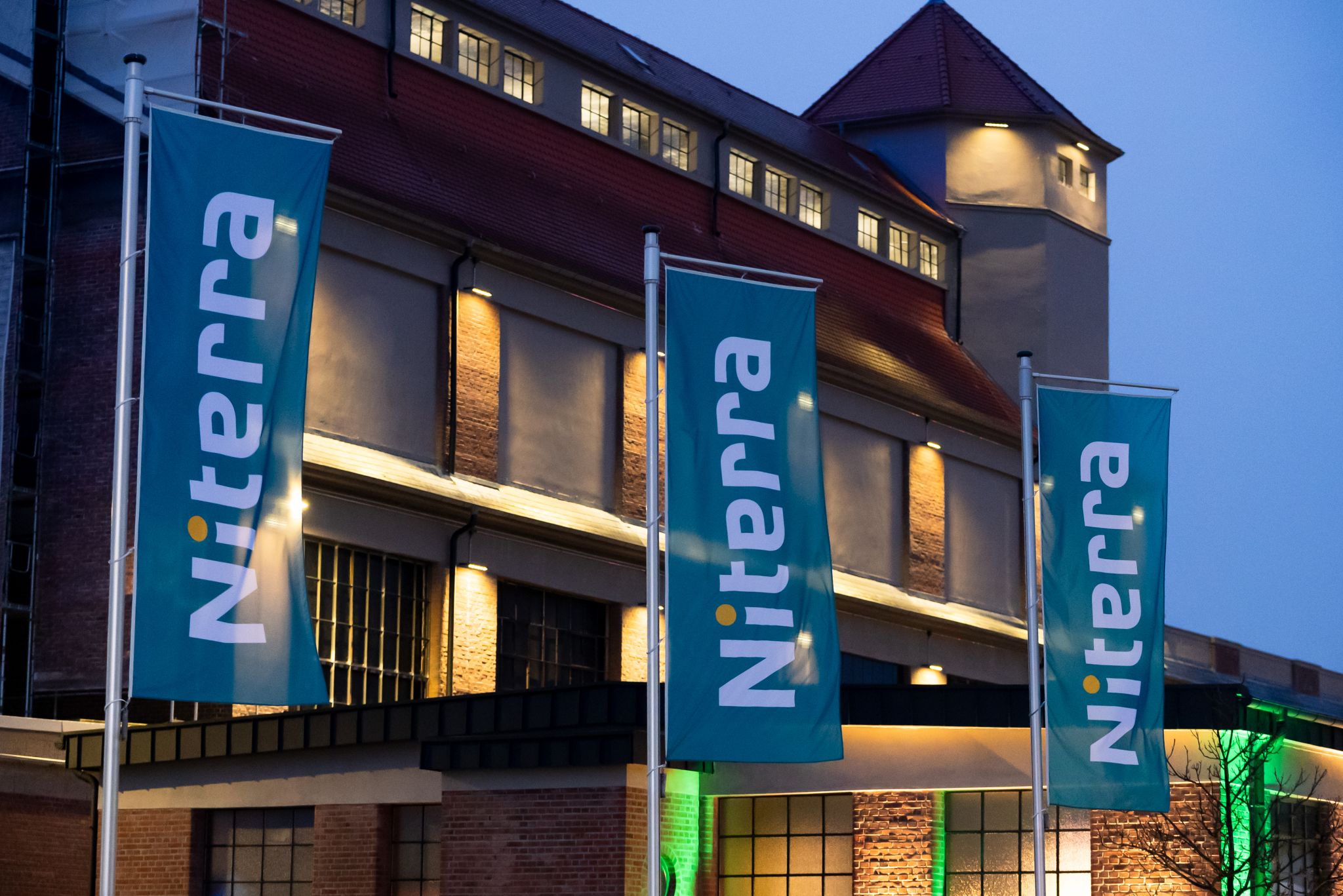 Drei große Niterra-Fahnen im Vordergrund des beleuchteten Firmengebäudes bei Dämmerung.