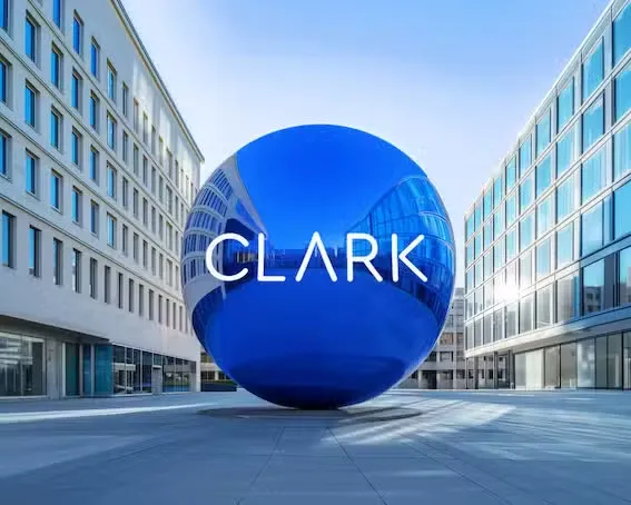 Eine große, glänzende blaue Kugel mit dem CLARK Logo steht auf einem Platz zwischen modernen Bürogebäuden.